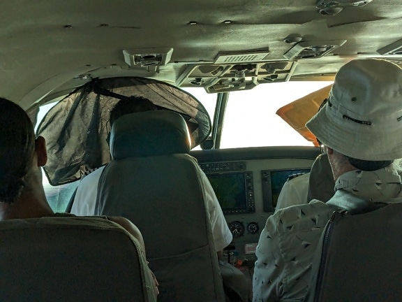 Pessoas sentadas em assentos de passageiros atrás do piloto em um pequeno avião comercial