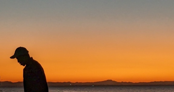 Silhouet van de mens die zich voor een zonsopgang met oranje gele hemel bevinden