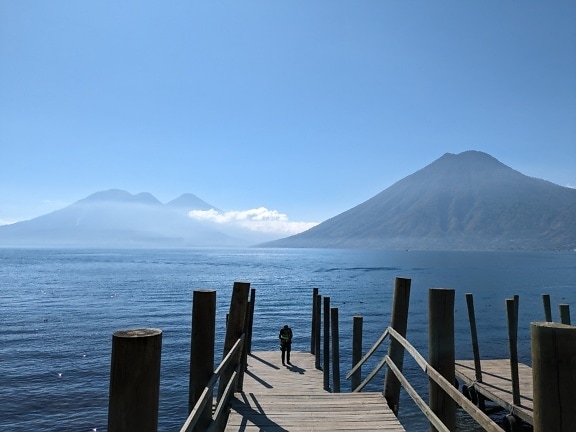 Egy fából készült dokkon álló személy, háttérben az Atitlán-tóval