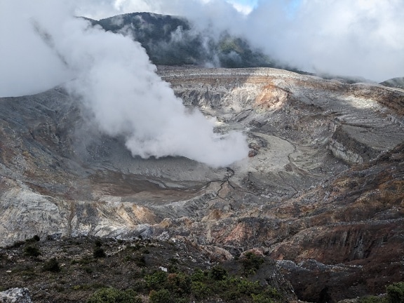 Landscape of Poás volcano crater in Costa Rica with smoke coming out of it