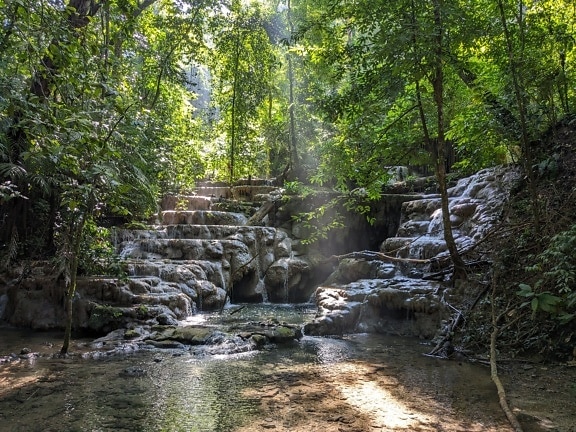 Majestätischer Wasserfall in einem tropischen Wald mit Sonnenstrahlen durch die Äste der Bäume