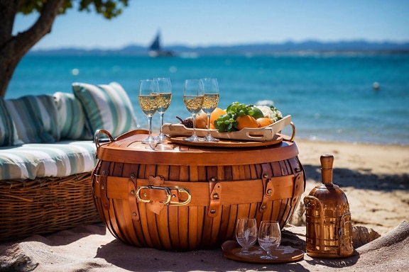 Piknikkosár pohár fehérborral és tálca gyümölcsökkel a strandon