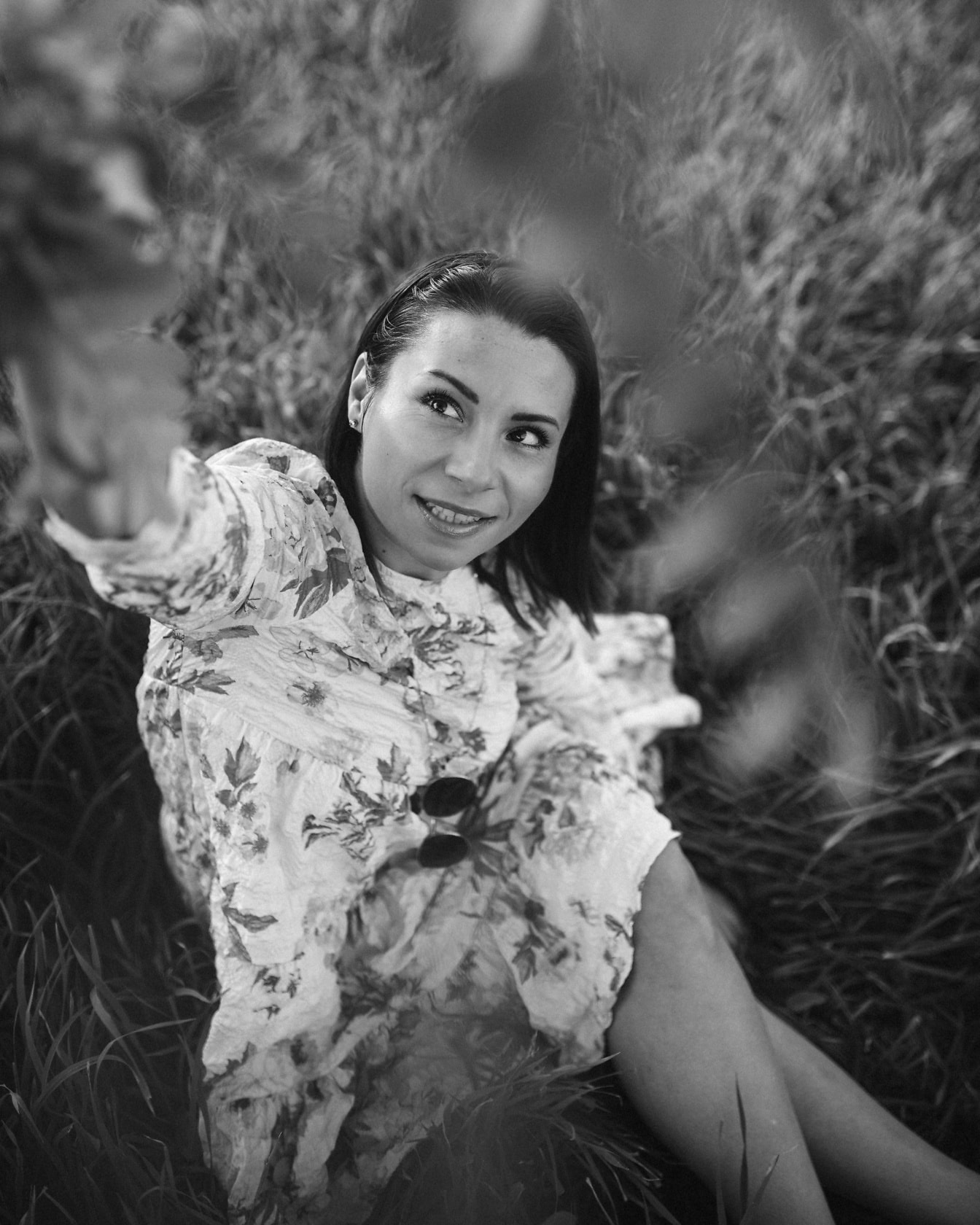 Fekete-fehér portré egy gyönyörű, mosolygós nőről, aki a fűben ül
