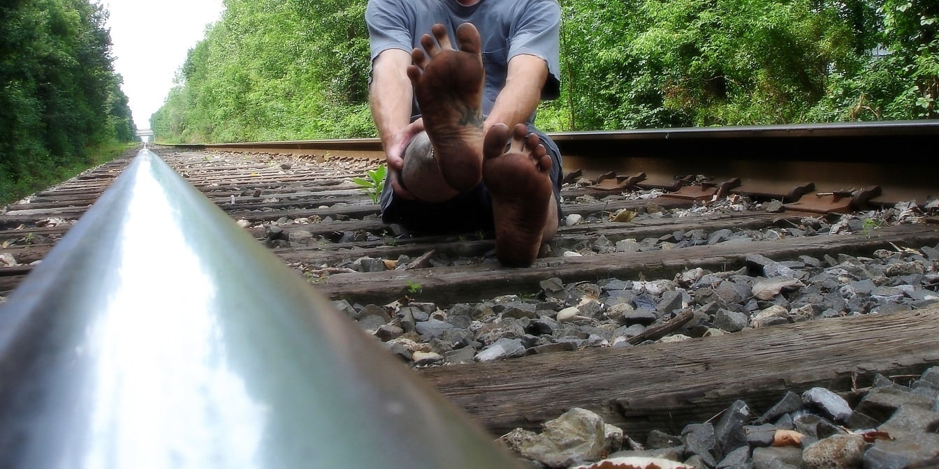 Bosy mężczyzna siedzi na torach kolejowych