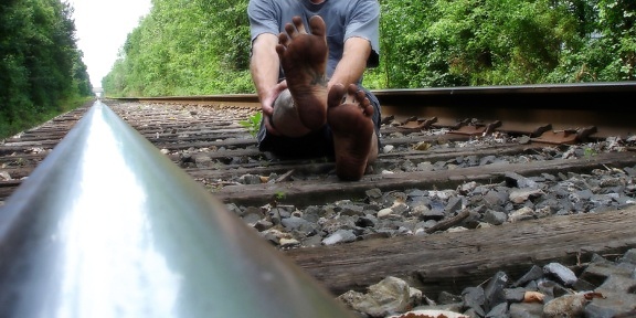 Barfüßiger Mann sitzt auf Bahngleisen