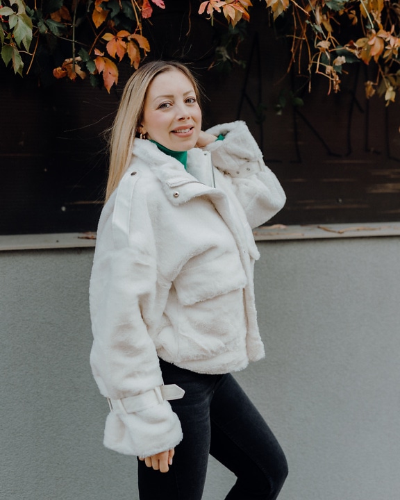 Beautiful young woman in a white fur coat posing standing
