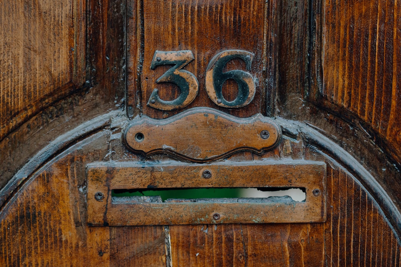 Kotak surat di pintu depan kayu dengan nomor logam di atasnya