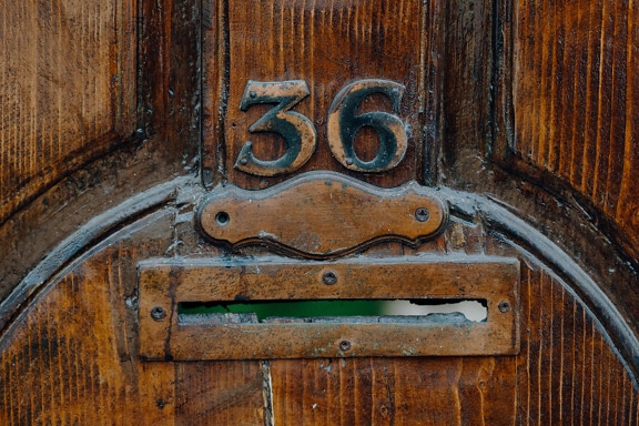 Mailbox on wooden front door with metal number above it