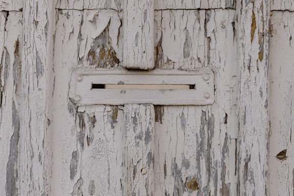 Mail slot on old wooden doors with peeling white paint