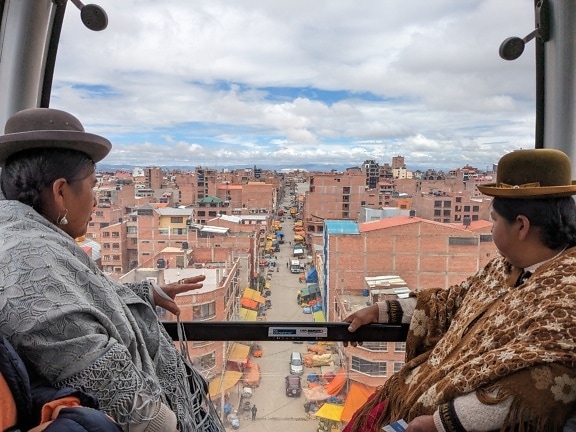 ผู้หญิงโบลิเวียสองคนนั่งกระเช้าลอยฟ้าและมองเห็นเมืองลาปาซในโบลิเวีย