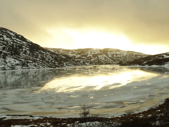 Zamrznuté jazero s hmlistými horami v pozadí pri východe slnka