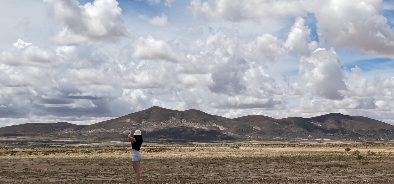 Wanita berdiri di padang pasir dengan pegunungan di latar belakang