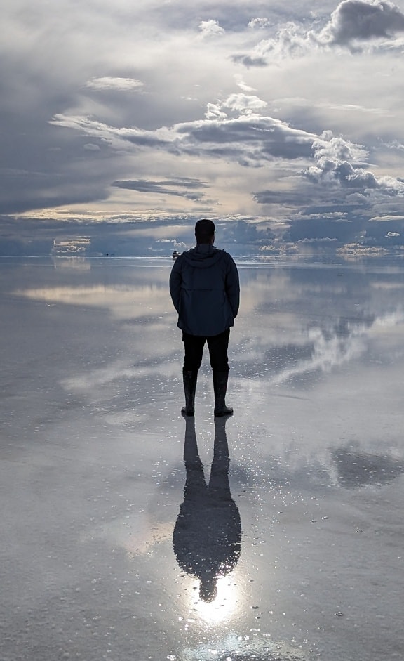 Ilusão de ótica do homem em pé sobre uma superfície de águas rasas