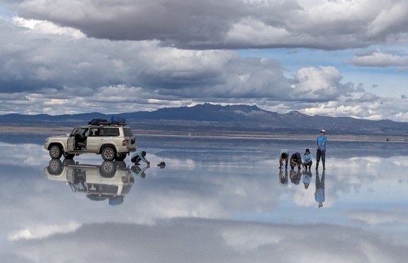 Ilusão de ótica de carro e pessoas em pé em uma superfície de lago