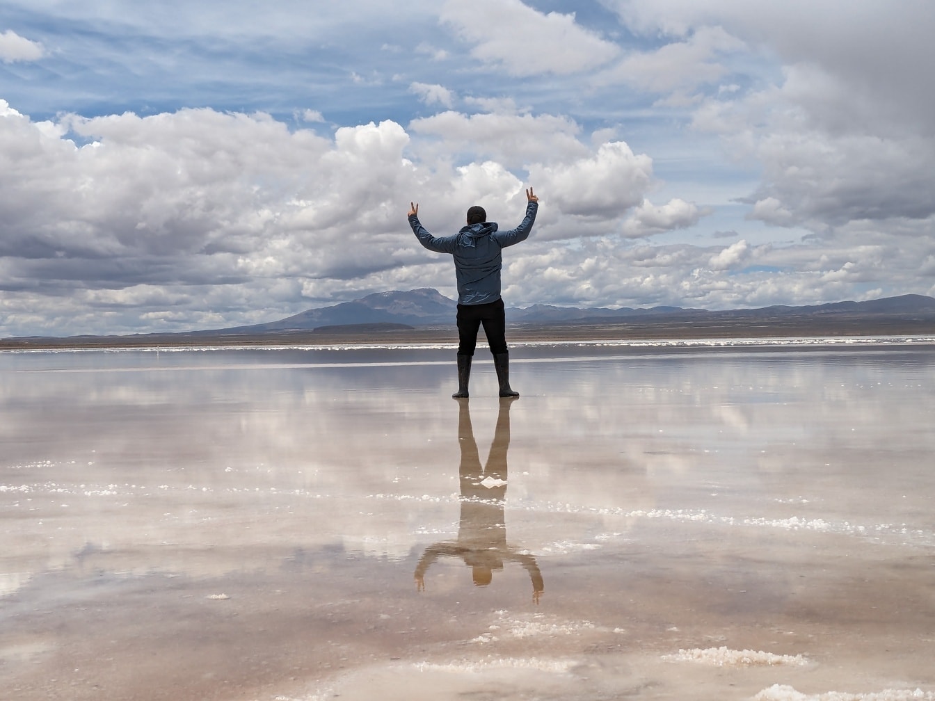 Čovjek ponosno stoji u slanom jezeru s podignutim rukama