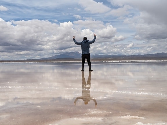 Pria dengan bangga berdiri di danau garam dengan tangan terangkat