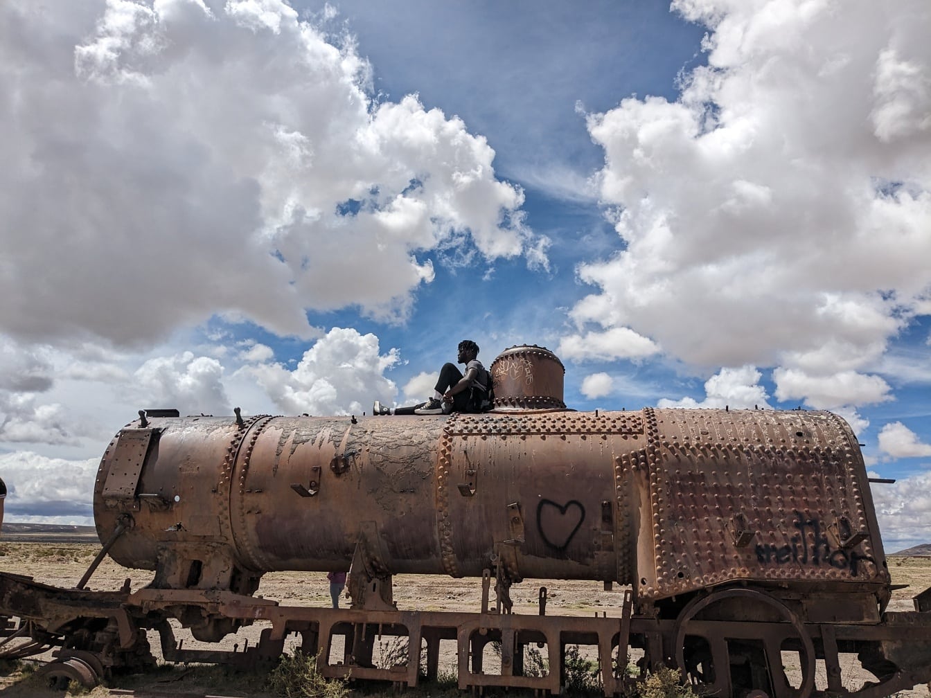 Person sitting on top of an old rusty train abandoned in the desert