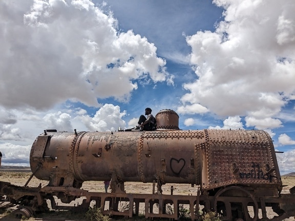 Человек, сидящий на крыше старого ржавого поезда, брошенного в пустыне