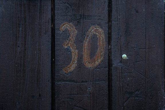 Nummer 30 auf einem vertikalen Holzbrett, das in dunkelbrauner Farbe gestrichen ist