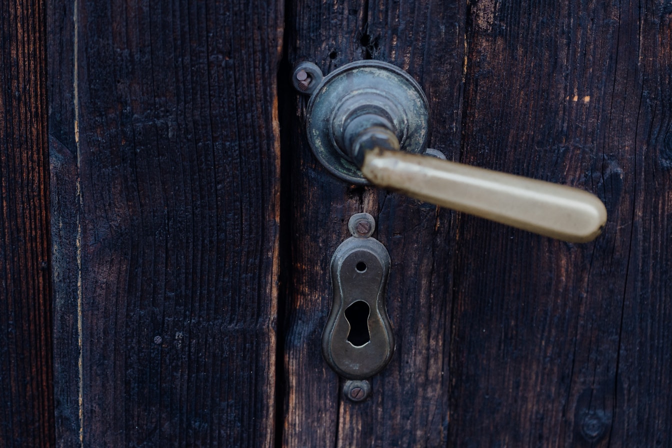 Postrzępiona klamka i dziurka od klucza na starych drewnianych drzwiach