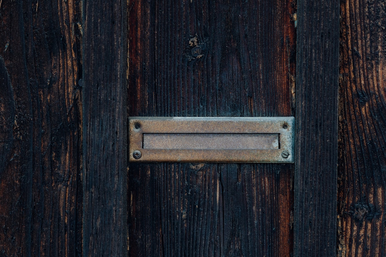 Метален пощенски слот на стари дървени врати, покрити с моторно масло