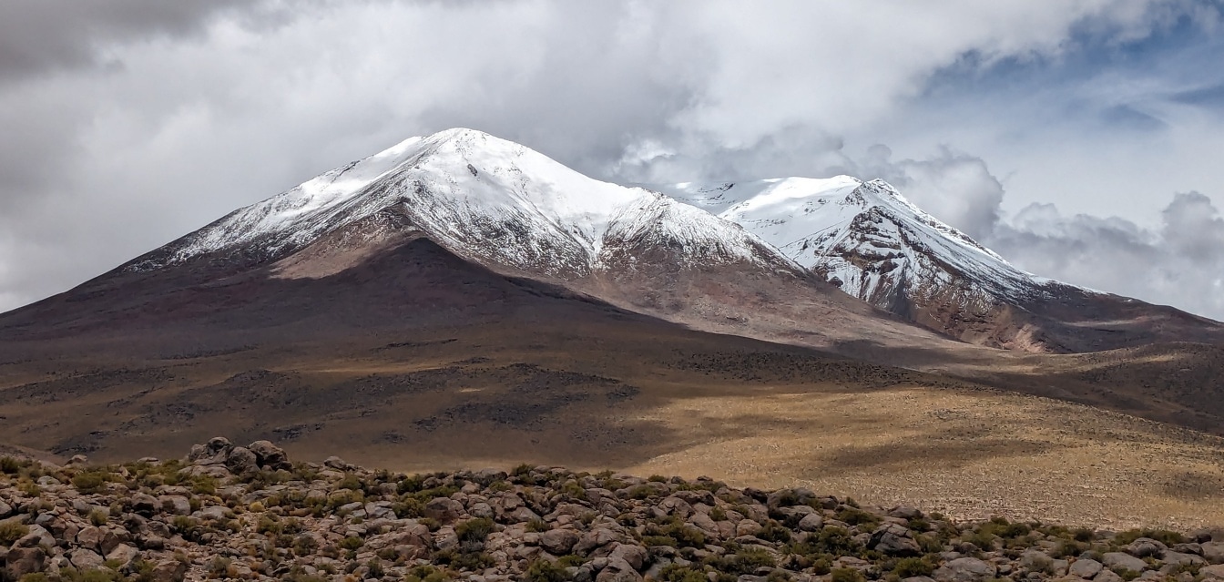 Snötäckta bergstoppar med ett platt fält framför sig i Atacamaöknen i Sydamerika