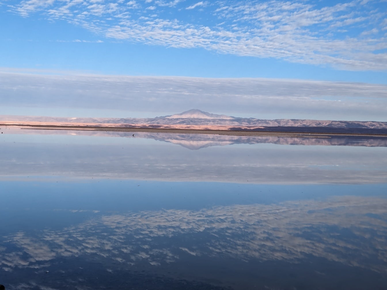 Refleksion af en blå himmel med skyer og bjerg i afstand i en salt sø