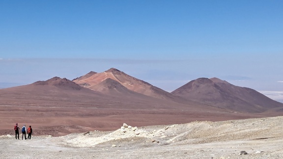 นักท่องเที่ยวเดินผ่านทะเลทรายในชิลีโดยมีภูเขาและท้องฟ้าสีครามเป็นฉากหลัง