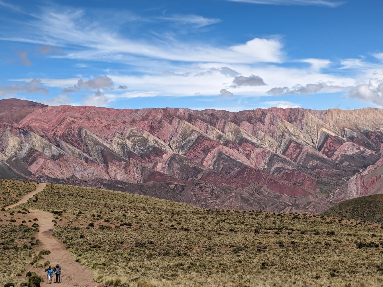 Туристы идут по грунтовой тропе перед горным хребтом в Серрания-де-Орнокаль в Аргентине