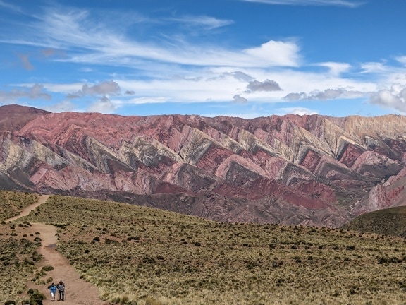 นักปีนเขาเดินบนเส้นทางลูกรังหน้าเทือกเขาใน Serranía de Hornocal ในอาร์เจนตินา