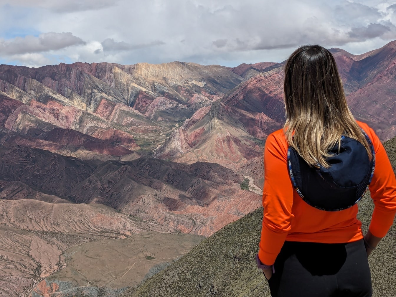 Eine umgedrehte Frau mit Hut auf dem Rücken steht auf dem Gipfel eines Berges und genießt das Panorama des Tals