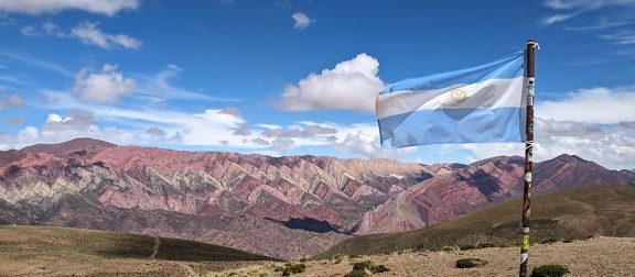 Знаме на Аржентина на ръждясал метален стълб, веещ се от вятъра в планината