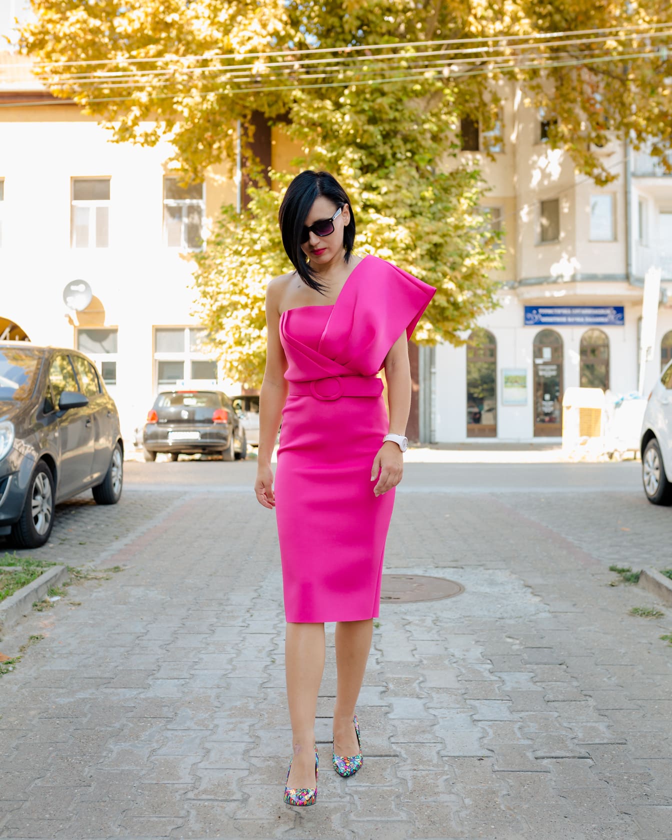 Elegantní žena v módních růžových šatech kráčející po ulici