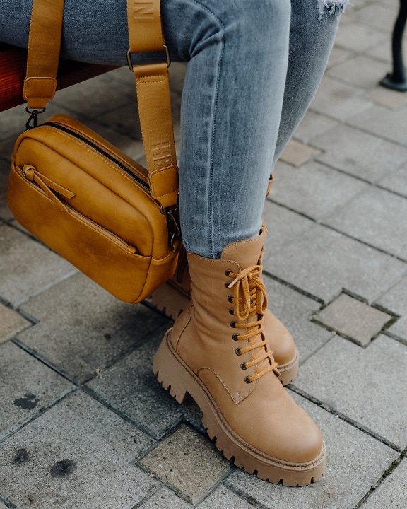 Women’s legs in fashionable jeans and leather winter boots next to a yellow leather bag