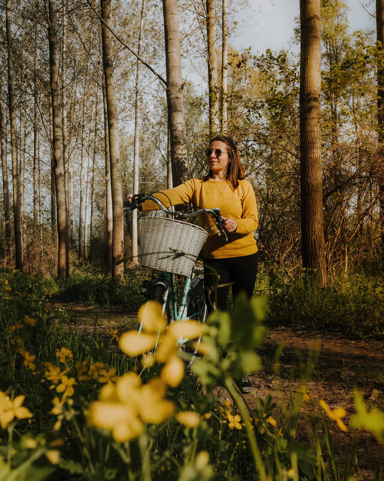Eine fröhliche Frau spaziert an einem sonnigen Frühlingstag mit ihrem Fahrrad auf dem Waldweg im Wald