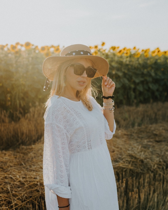 Country woman in a white folk dress and hat in a field of sunflowers at sunny summer day