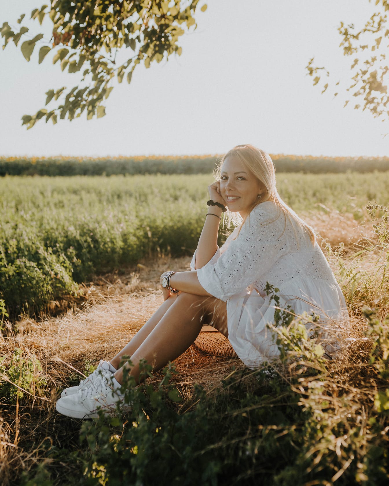 Kaunis hymyilevä maalaisnainen istuu pellolla aurinkoisena kesäpäivänä