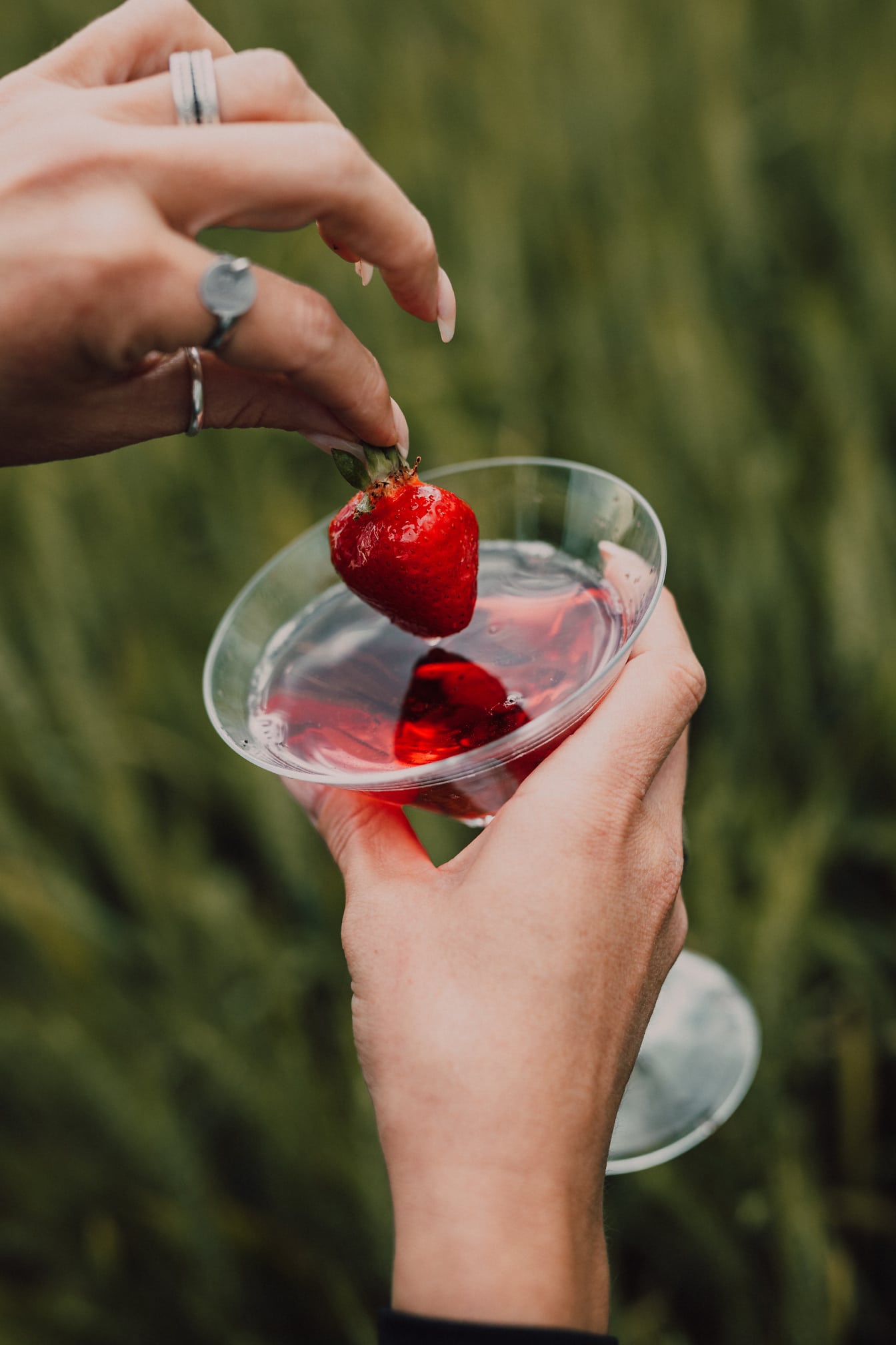 A hand who removes a strawberry from a strawberry cocktail