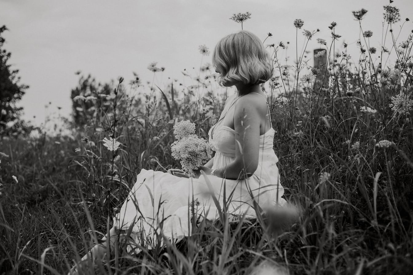 Portret alb-negru al miresei de la țară așezată într-un câmp de flori