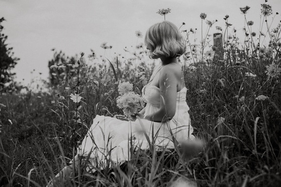 Чорно-білий портрет сільської нареченої, що сидить у полі квітів