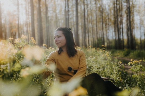 En kvinne sitter i en blomstereng i skogen en solrik vårdag