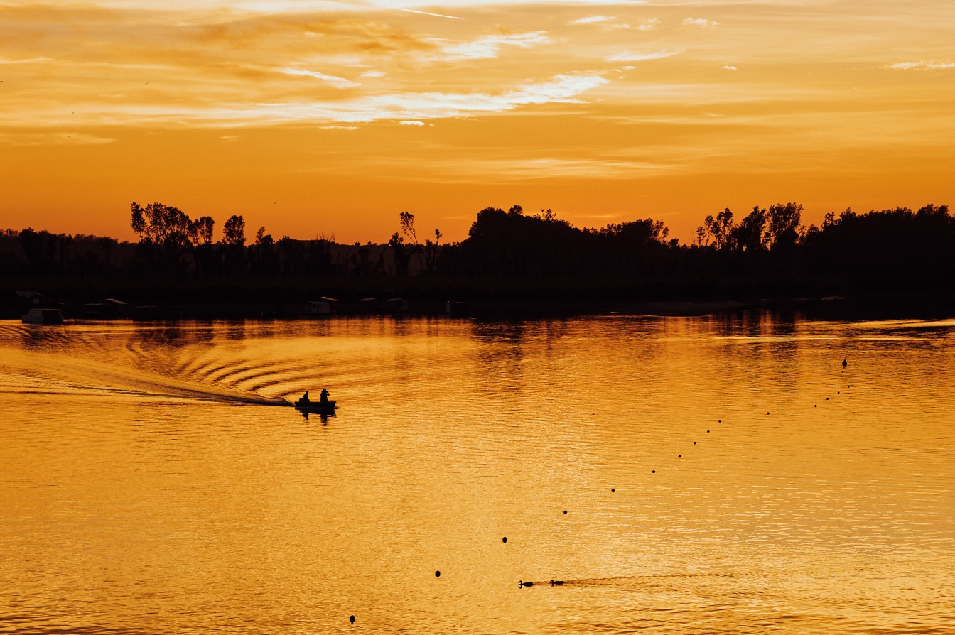 Silhuett av to personer i en båt på en innsjø med en dramatisk oransje solnedgang som bakgrunn
