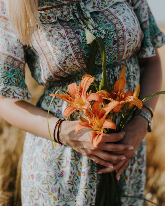 A woman in a floral dress holds a bouquet of orange amaryllis flowers