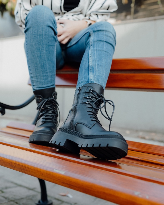 A person who sitting on a bench and wears brand new black leather boots