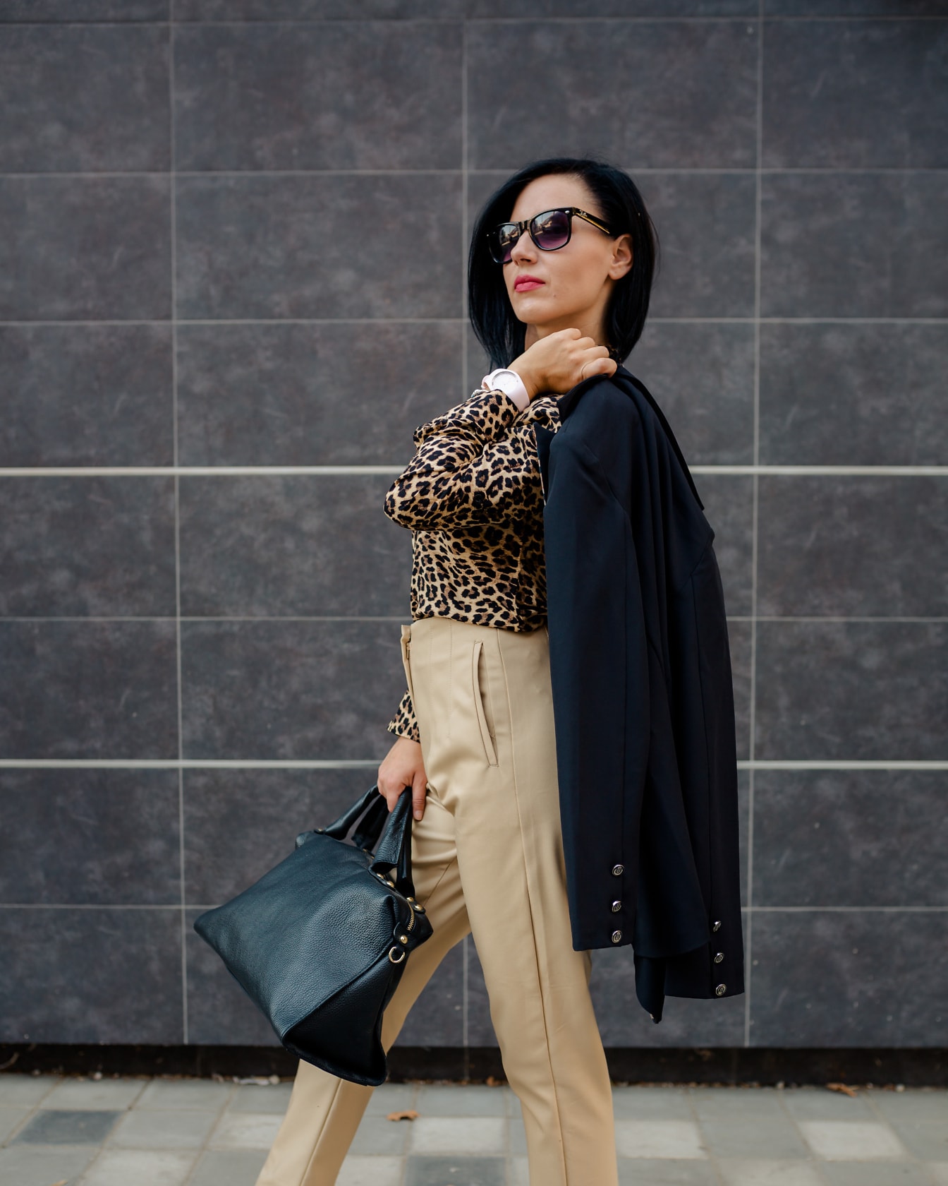 Femeie de afaceri încrezătoare, în cămașă cu imprimeu leopard și pantaloni bej, ținând în mână o geantă neagră