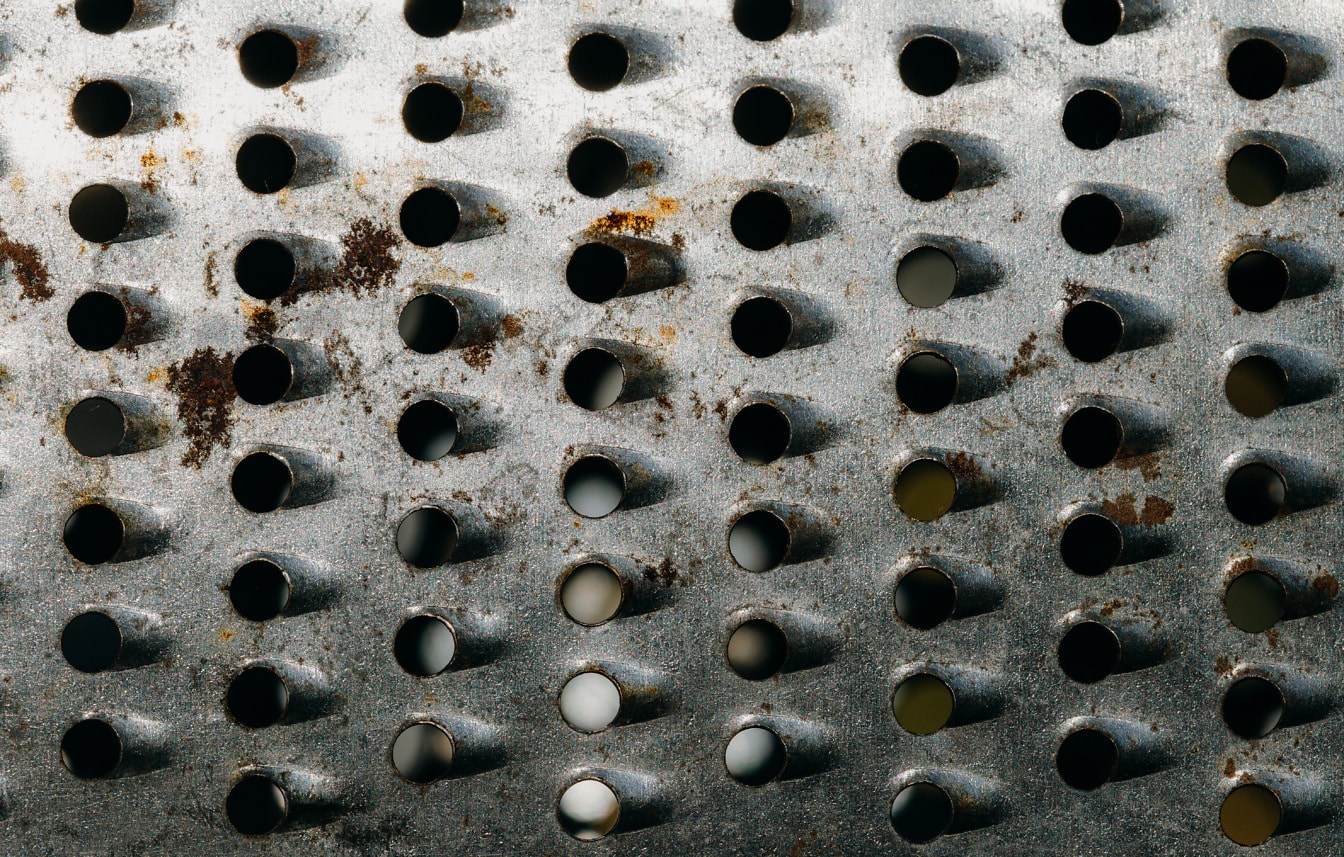 Rusten metaloverflade med mange små cirkelhuller af håndrivejern