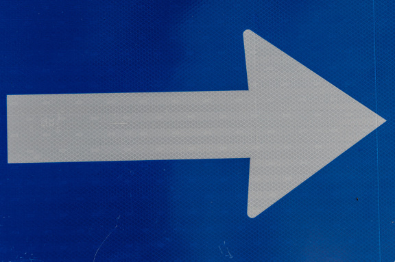 Señal de tráfico con flecha blanca hacia la derecha sobre superficie reflectante fluorescente azul oscuro