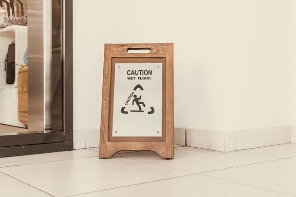 Wooden sign on the floor tiles with an inscription, caution wet floor