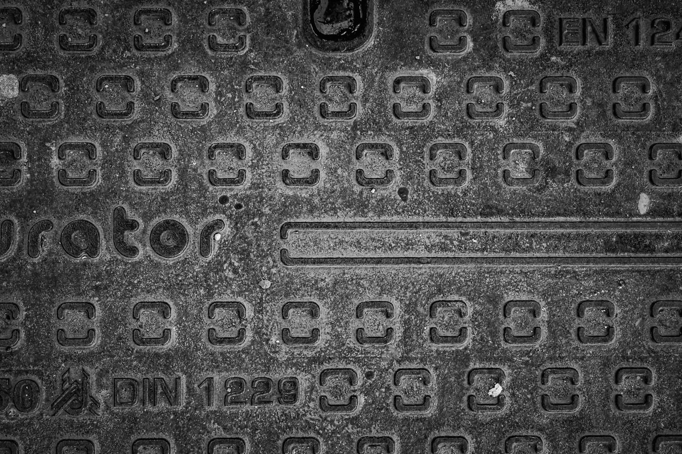Black and white texture of metal surface of cast iron manhole cover