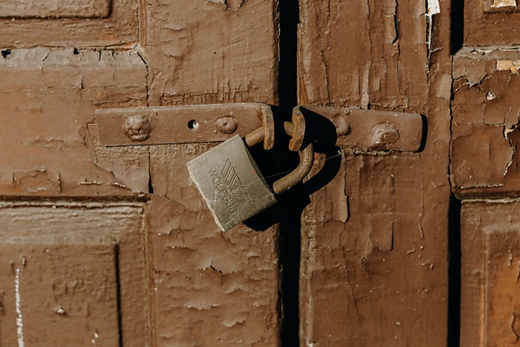 Rusty padlock on a wooden front door painted in brown